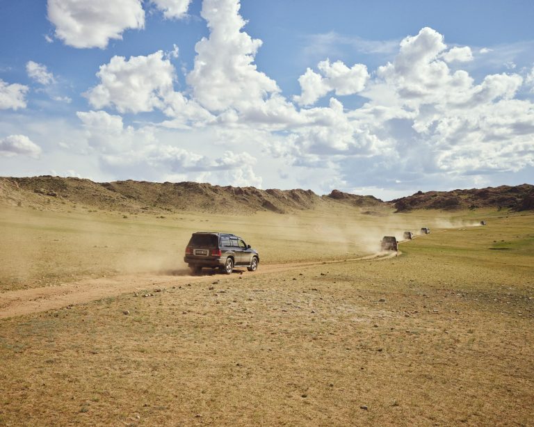Convoi de 4x4 roulant sur une piste poussiéreuse dans un paysage aride en Mongolie