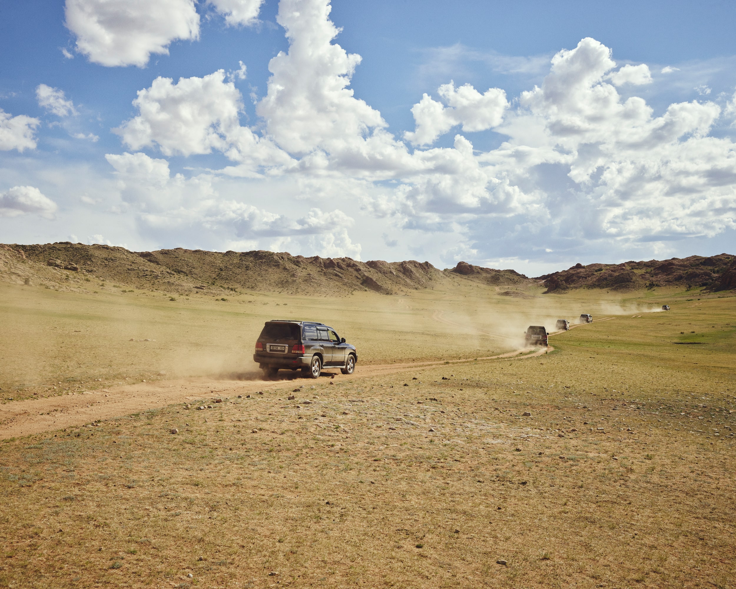 Convoi de 4x4 roulant sur une piste poussiéreuse dans un paysage aride en Mongolie